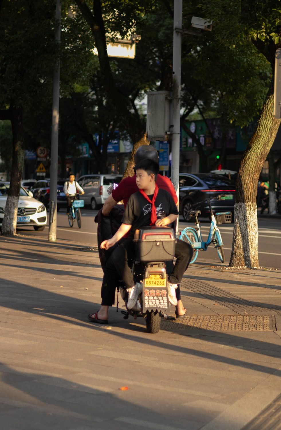 Boy with a red scarf riding on the back of a scooter in low evening sun